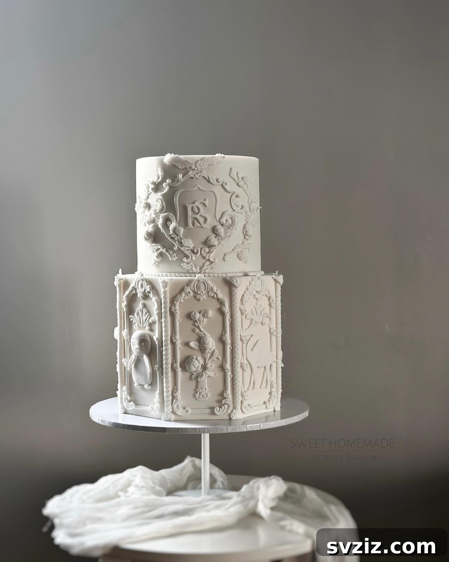 27 Elegant Wedding Cake Inspirations 12 A stunning white wedding cake featuring the elegant design of intertwined initials (R and S) as a beautiful focal point, adorned with intricate details and presented on a raised silver cake stand.