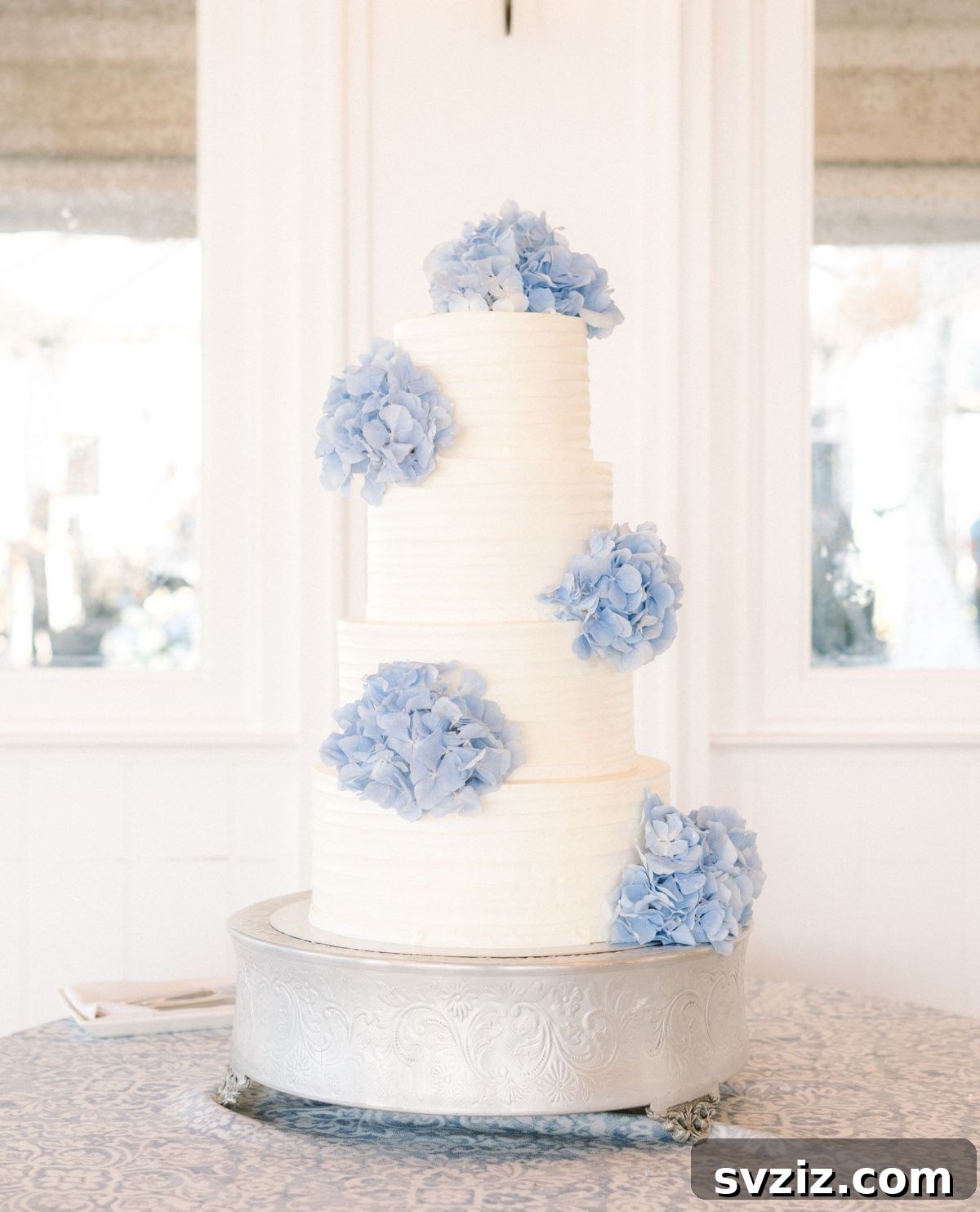 27 Elegant Wedding Cake Inspirations 18 A magnificent four-tier wedding cake adorned with beautiful blue hydrangeas, adding a classic and timeless touch, offering diverse flavor options for guests, ideal for a garden-inspired wedding.