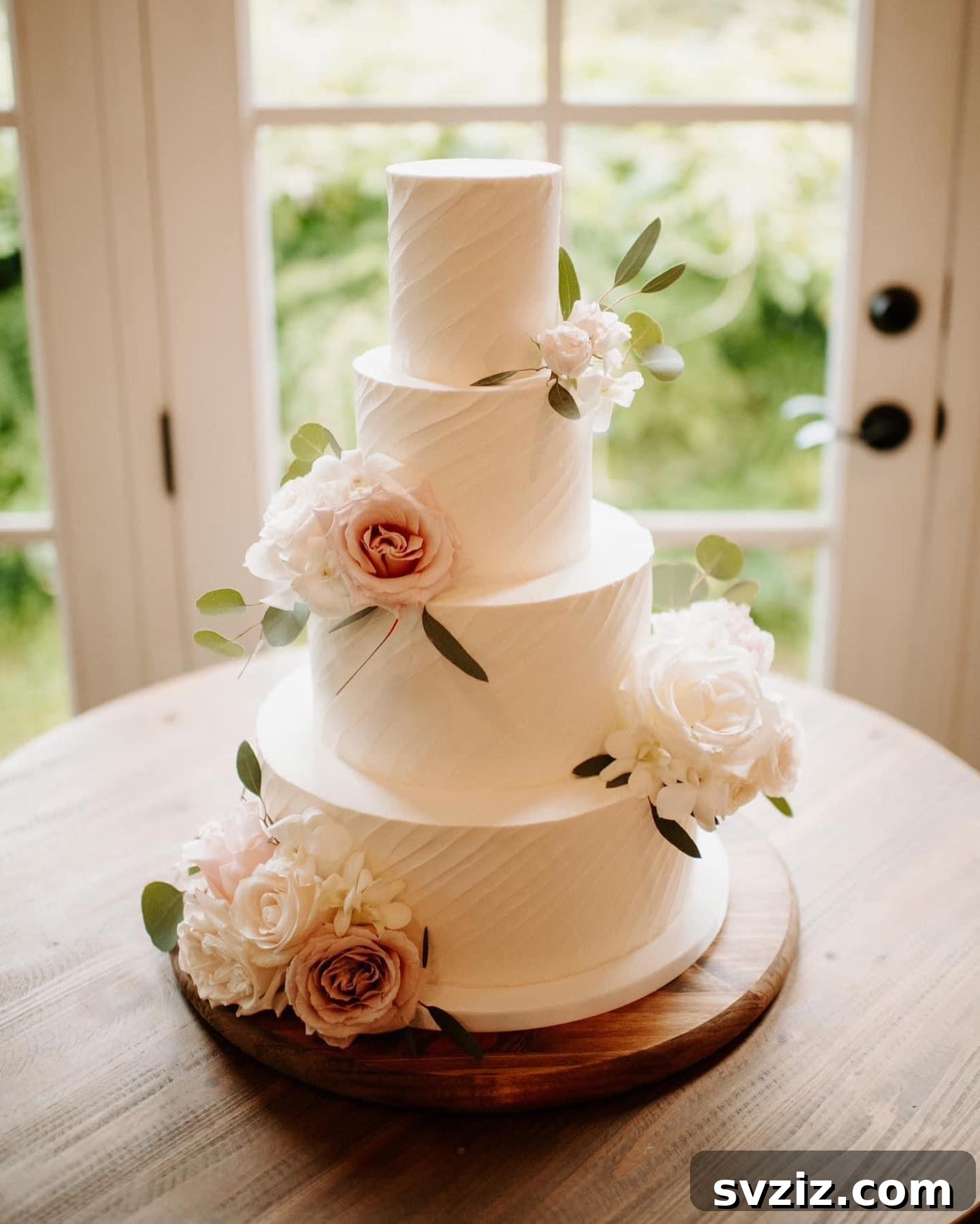 27 Elegant Wedding Cake Inspirations 3 A four-tier wedding cake adorned with delicate blush pink roses, perfect for a classic and romantic celebration. This elegant vanilla bean cake promises timeless beauty and delicious flavor.