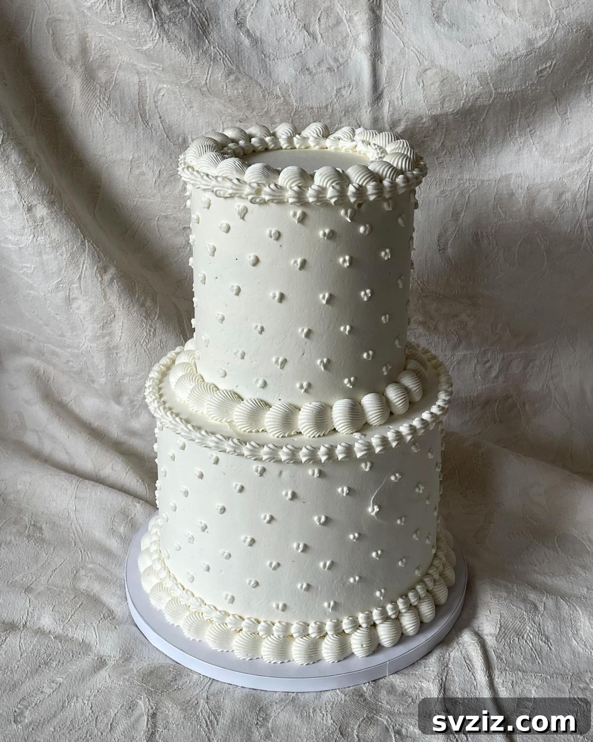 27 Elegant Wedding Cake Inspirations 23 A glorious two-tier wedding cake adorned with countless tiny piped hearts, symbolizing love, with each tier consisting of four layers, offering a large canvas for decoration, highlighted by a heart-shaped piping tool.