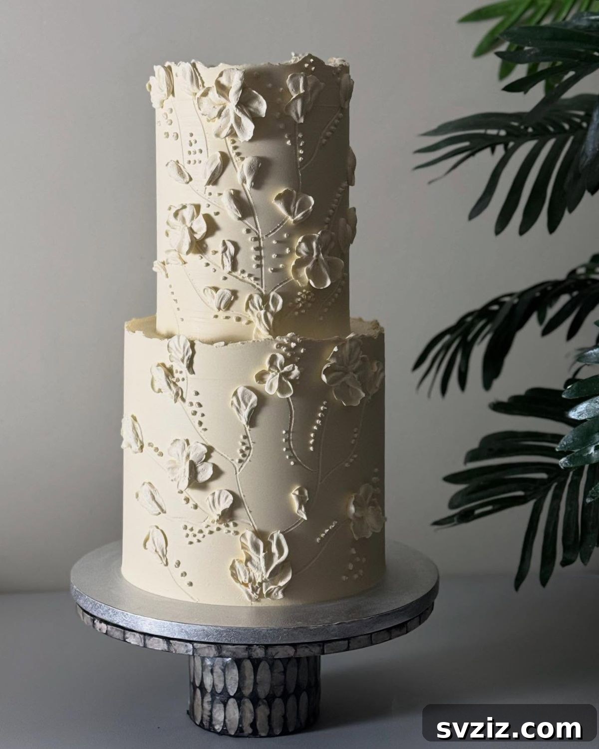 27 Elegant Wedding Cake Inspirations 28 An intricate wedding cake showcasing embroidered lace illusion with elaborate blooms, vines, leaves, and petals, featuring raw-edged detailing for organic charm, whispering of love and quiet sophistication.