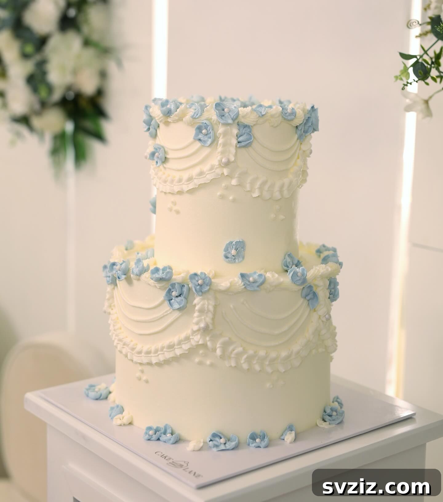 27 Elegant Wedding Cake Inspirations 29 A stunning wedding cake resembling a bridal gown, with a sculpted corset-like top tier and a graceful skirt-like lower tier draped in lace, adorned with a charming arrangement of blue hydrangeas.