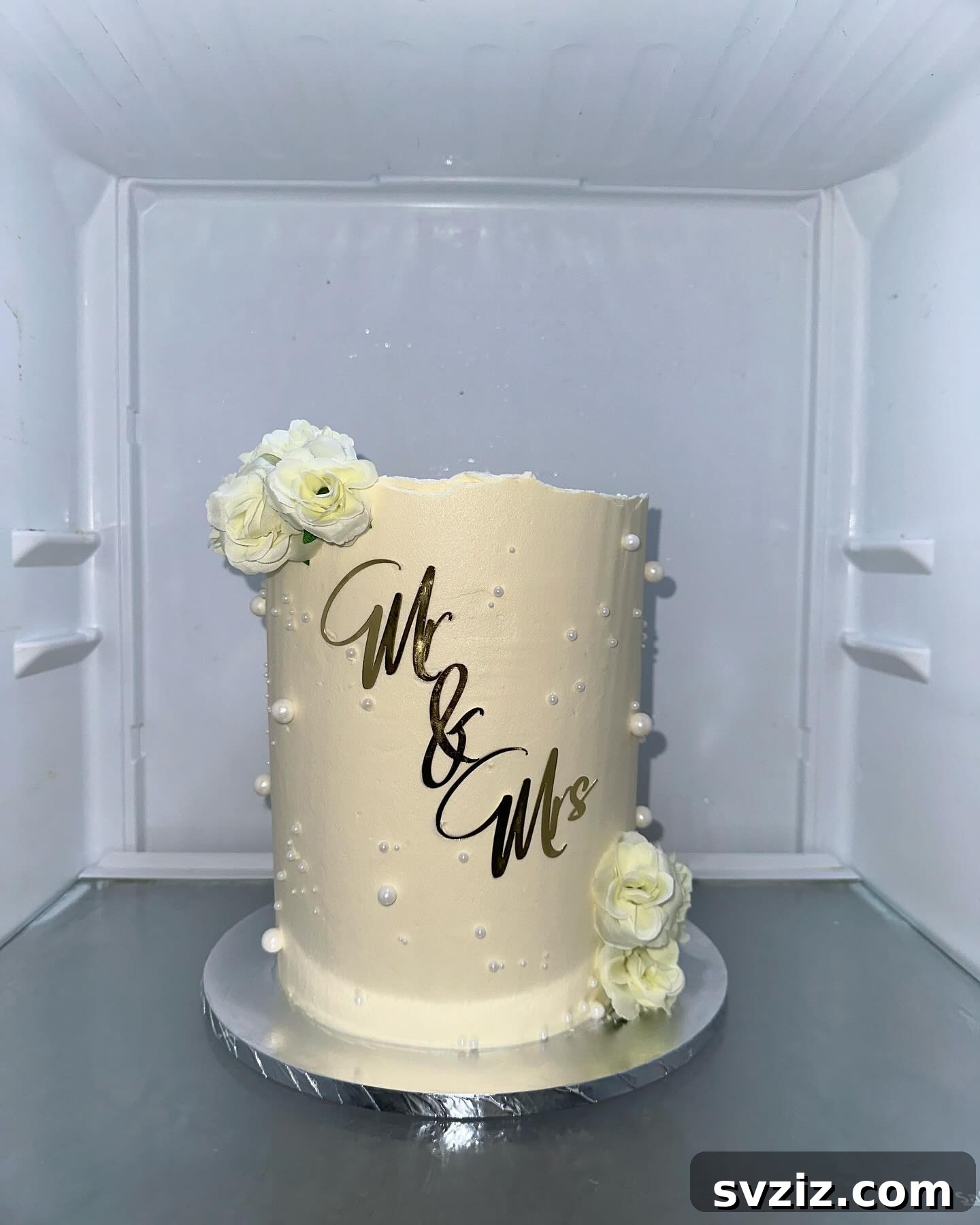27 Elegant Wedding Cake Inspirations 5 An elegant single-tier white wedding cake featuring two bouquets of white roses, shimmering pearlescent accents, and a glorious golden Mr & Mrs sign, symbolizing a new journey.