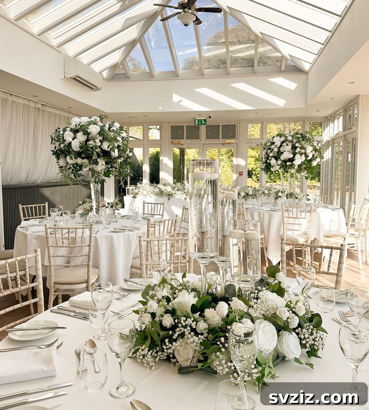 Dreamy sunlit garden pavilion wedding reception with towering white floral centerpieces and natural tones.