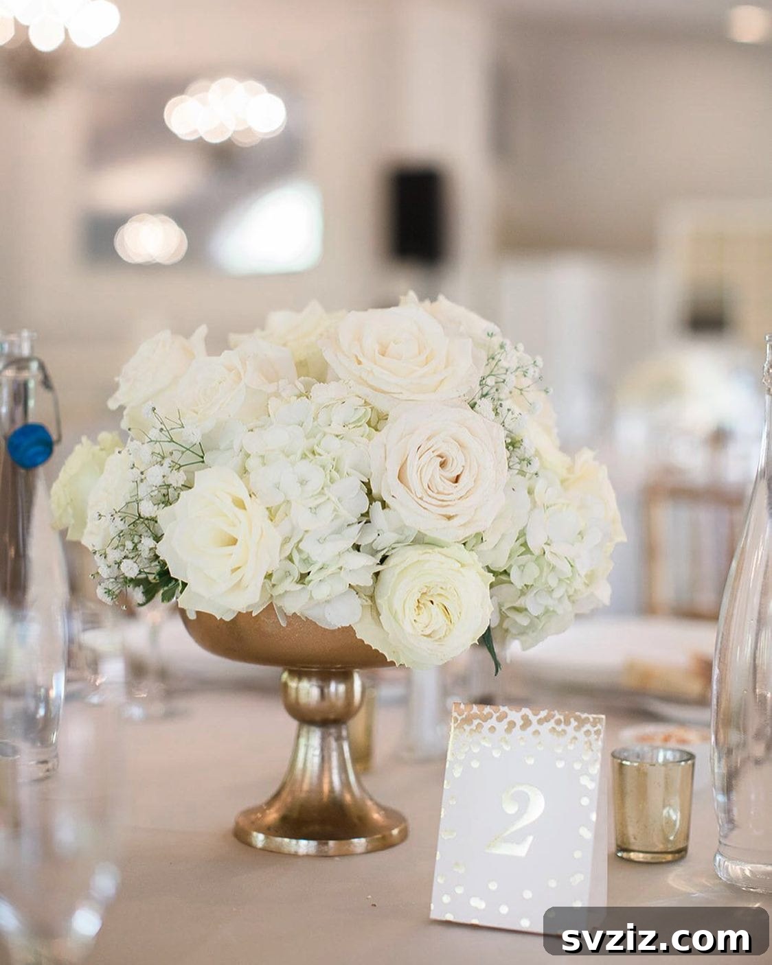 Romantic white rose centerpiece in an opulent gold vase, featuring subtle greenery for a classic wedding table.