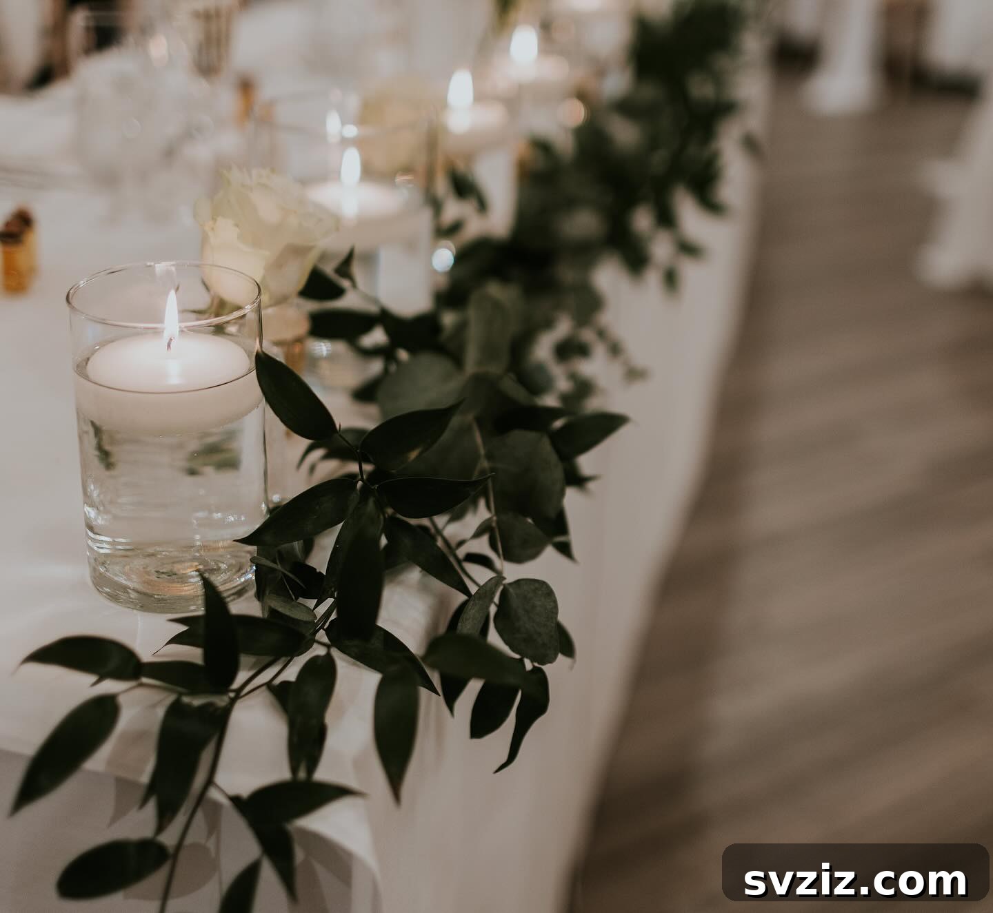 Elegant wedding table decor in green and soft white, featuring floating candles, fresh greenery, and white roses.