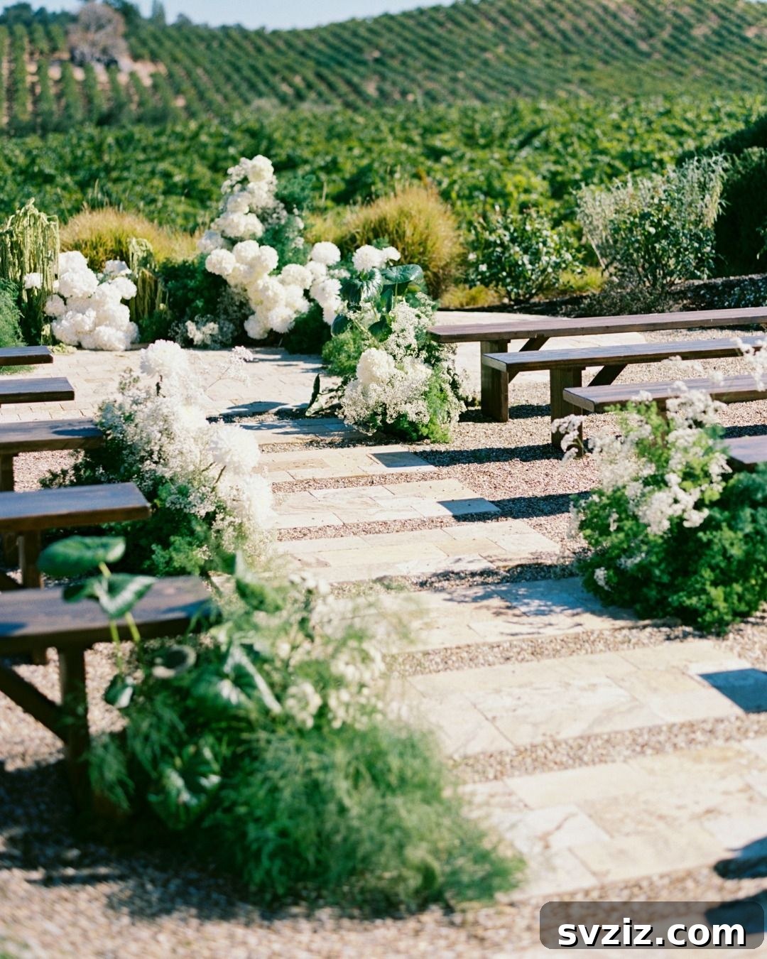 Romantic vineyard wedding ceremony setup with rustic wooden bench seating and lush floral arrangements.