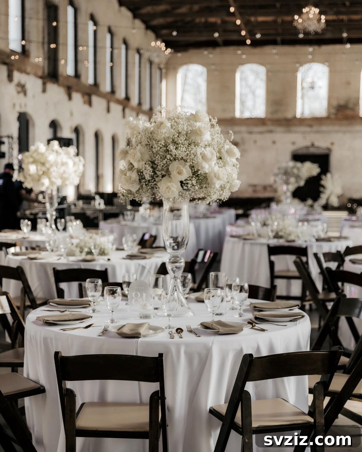 Rustic industrial wedding venue decor featuring exposed brick, high ceilings, and elegant white floral centerpieces.