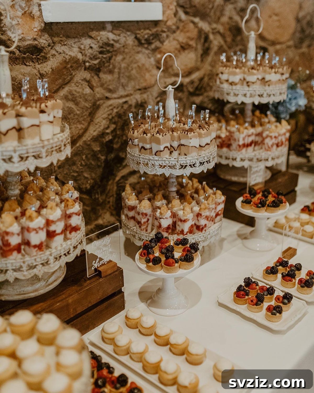 Exquisite Wedding Dessert Spreads 20 An opulent and elegant dessert table offering a tempting array of treats, from chocolate-layered shooters to berry-topped tarts, against a stone wall.