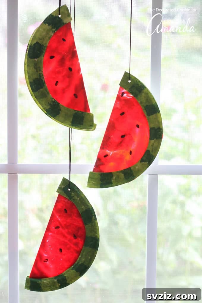 Vibrant watermelon suncatchers made from melted crayons, displaying red, white, and green segments with black seeds, perfect for summer decor.