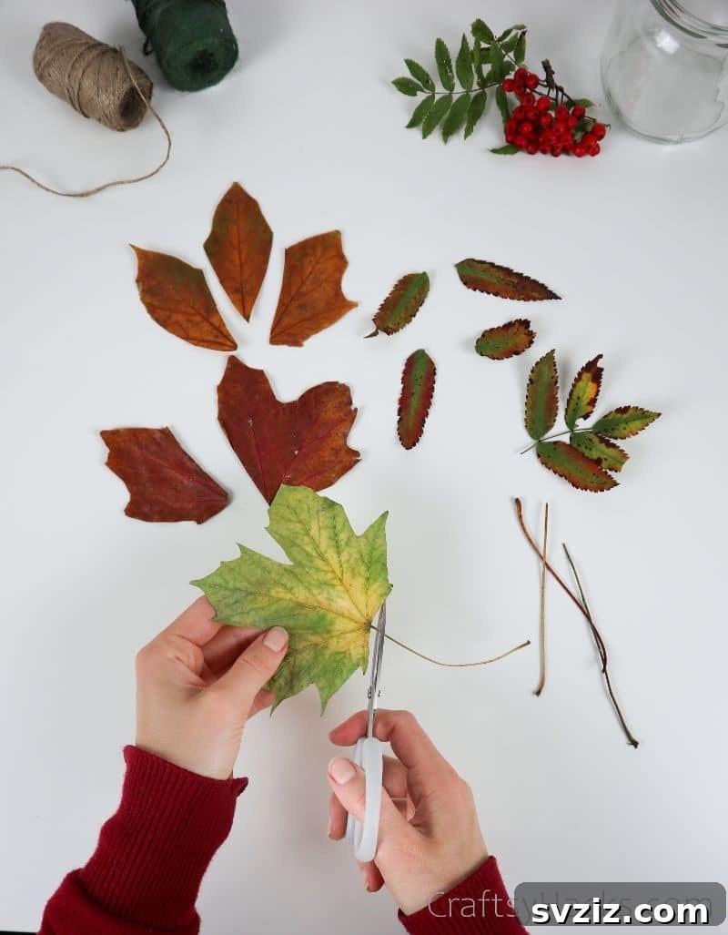 A hand cutting the stem off a faux leaf, demonstrating preparation for attaching it to the jar.