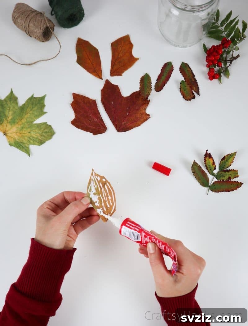 A hand applying glue to the back of a prepared autumn leaf, showcasing the adhesive application process.