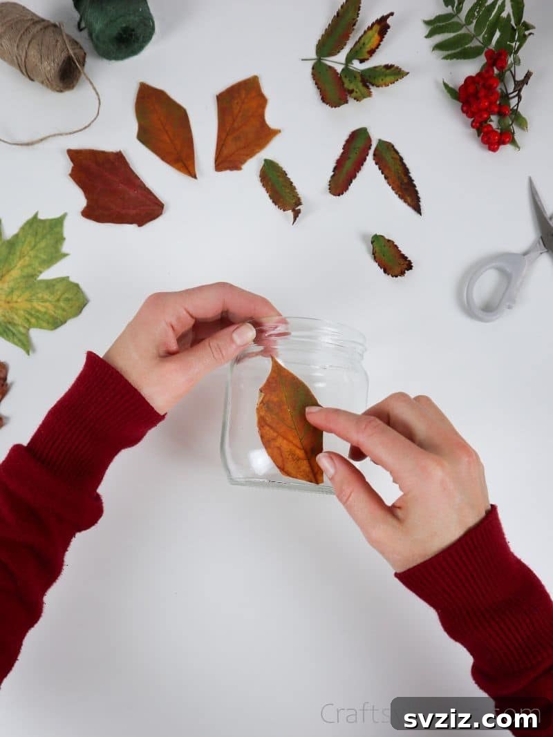 A hand carefully pressing a glued leaf onto the curved surface of a glass jar, ensuring smooth adhesion.