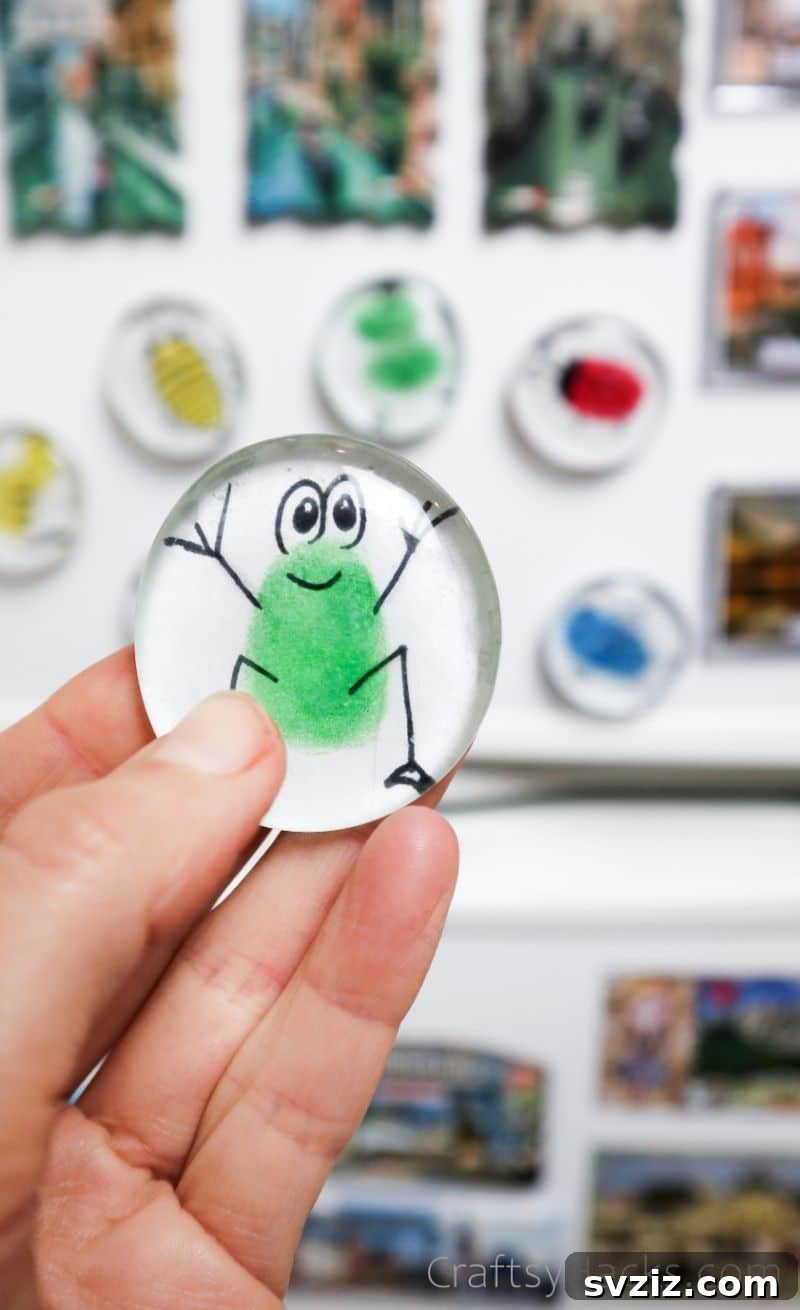 Fingerprint Keepsake Glass Magnets 2 Holding a DIY glass magnet featuring a cute frog figure made from a child's fingerprint, perfect for fridge decoration.
