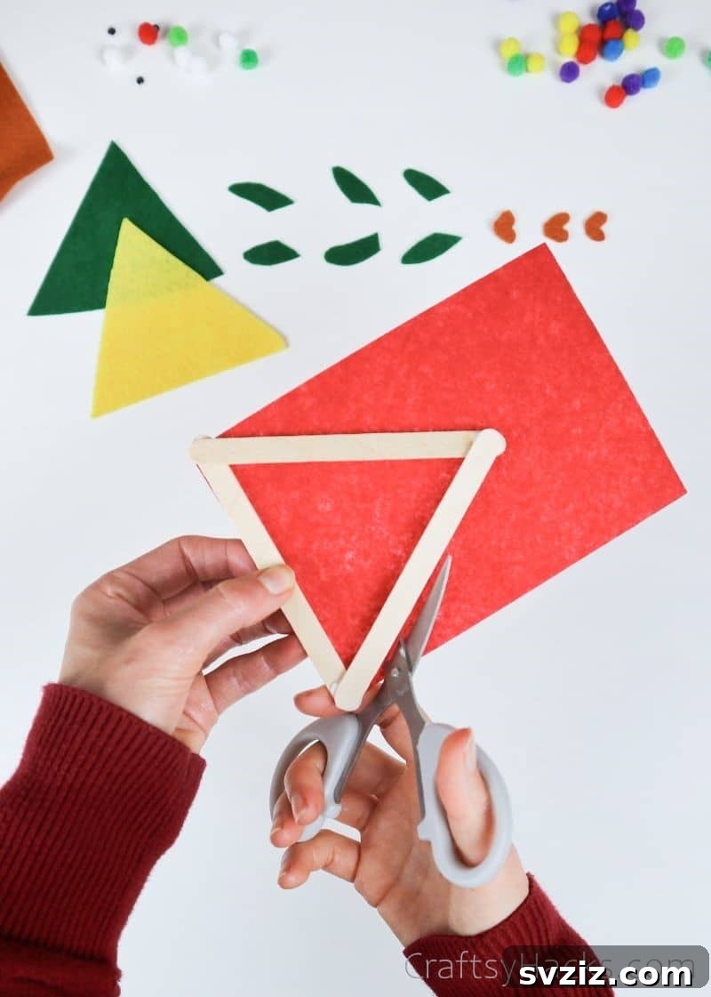 Simple Fish Crafts Kids Love to Make at School 7 Hands carefully cutting felt around a popsicle stick triangle to create the fish body.