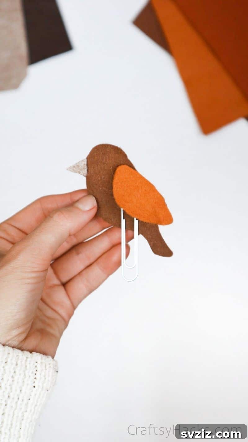 Creative Paper Clip Bookmarks 12 A hand holding a partially assembled felt bird bookmark, showing how the paperclip is secured