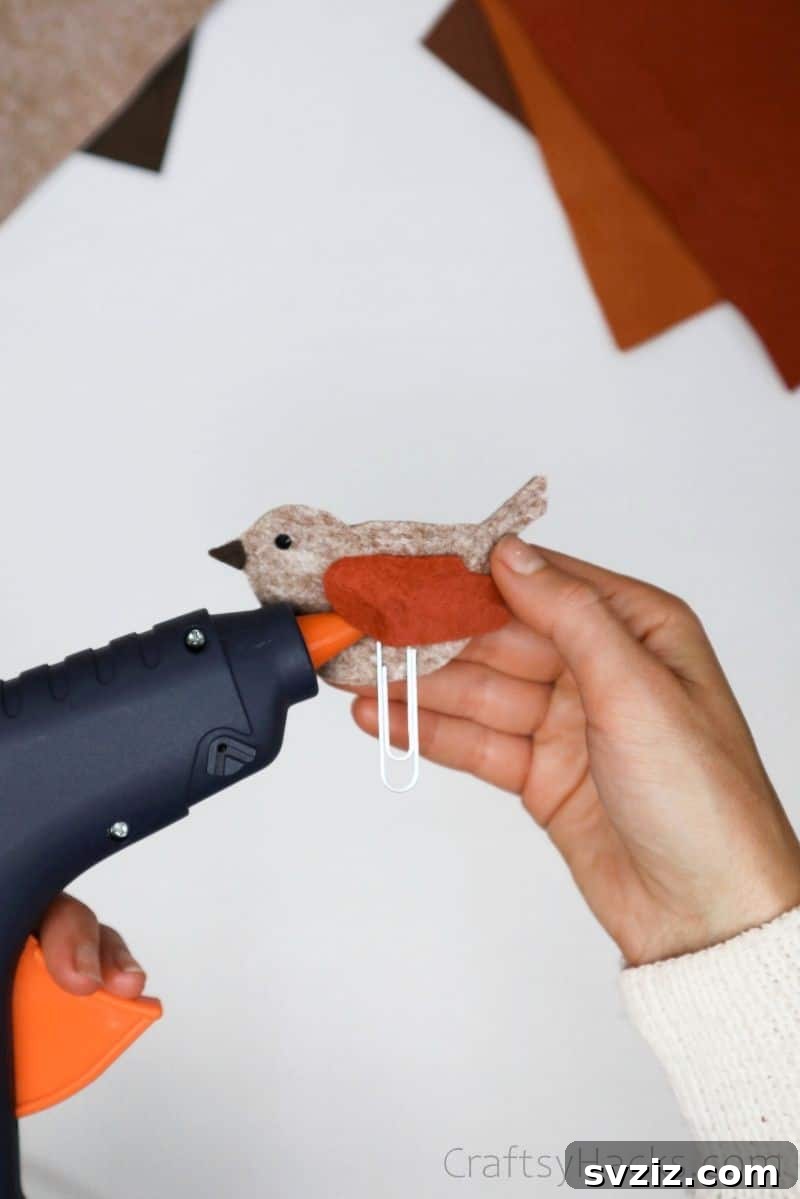 Creative Paper Clip Bookmarks 15 A hand applying a small amount of glue to attach a felt wing to the bird bookmark
