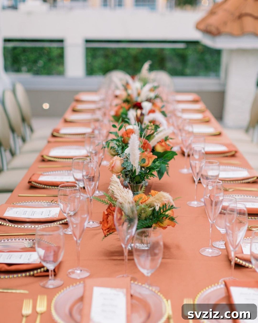 Stunning wedding table with coral linen, coral and peach rose centerpieces, gold beaded dinnerware, and pampas grass.